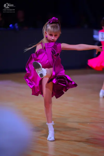 Dancesport competitor: Female dancer in foreground: magenta satin dress with large, structural ruffled 