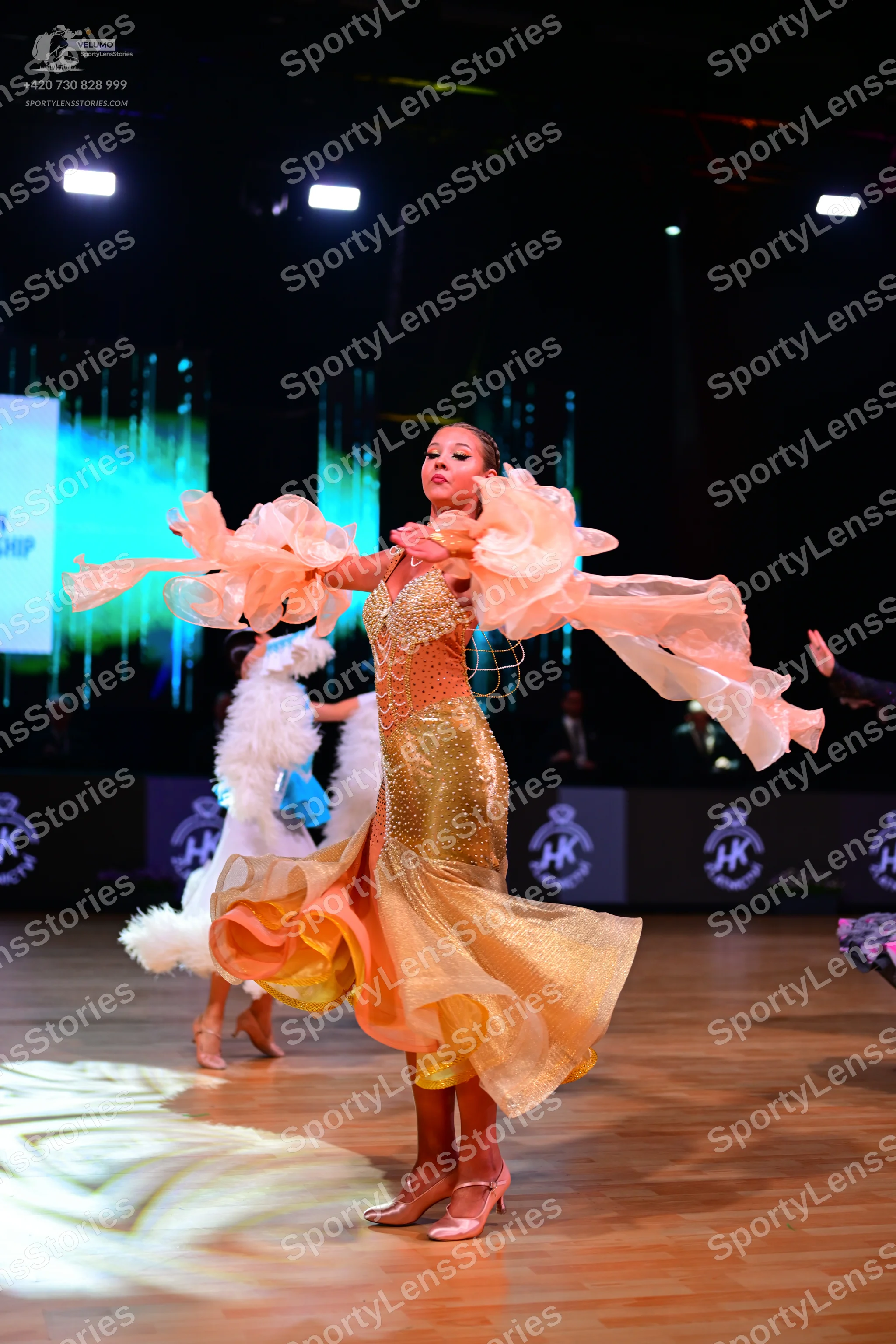 Dancesport competitor: Female dancer in foreground: gold/champagne ballroom gown with a shimmering, seq