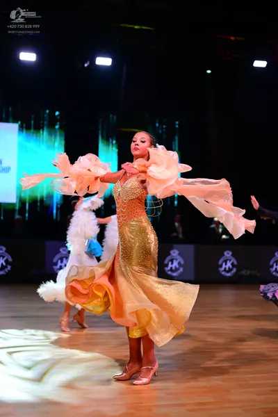 Dancesport competitor: Female dancer in foreground: gold/champagne ballroom gown with a shimmering, seq