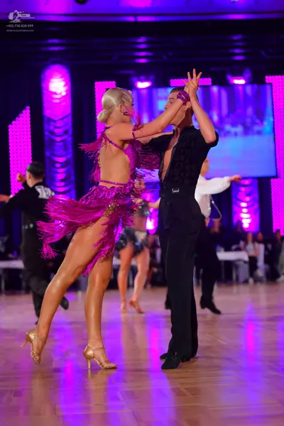 Dancesport competitor: Female dancer: magenta/purple Latin dress with long fringe and gold sequin embel