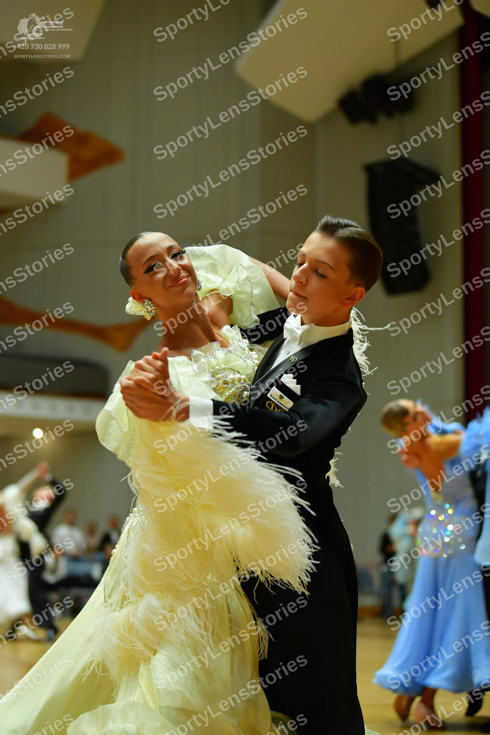 Dancesport competitor: Female dancer: pale yellow voluminous ballgown with ruffles and feathers, and la