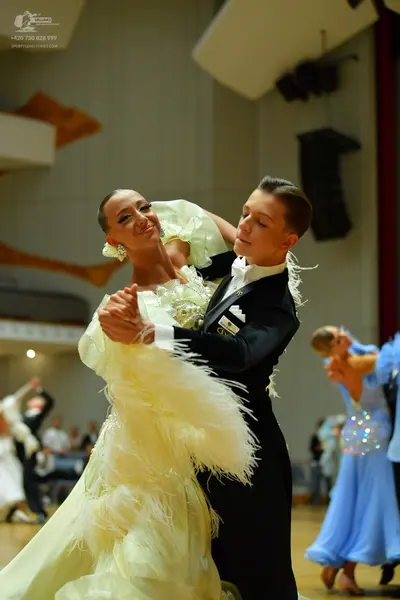 Dancesport competitor: Female dancer: pale yellow voluminous ballgown with ruffles and feathers, and la