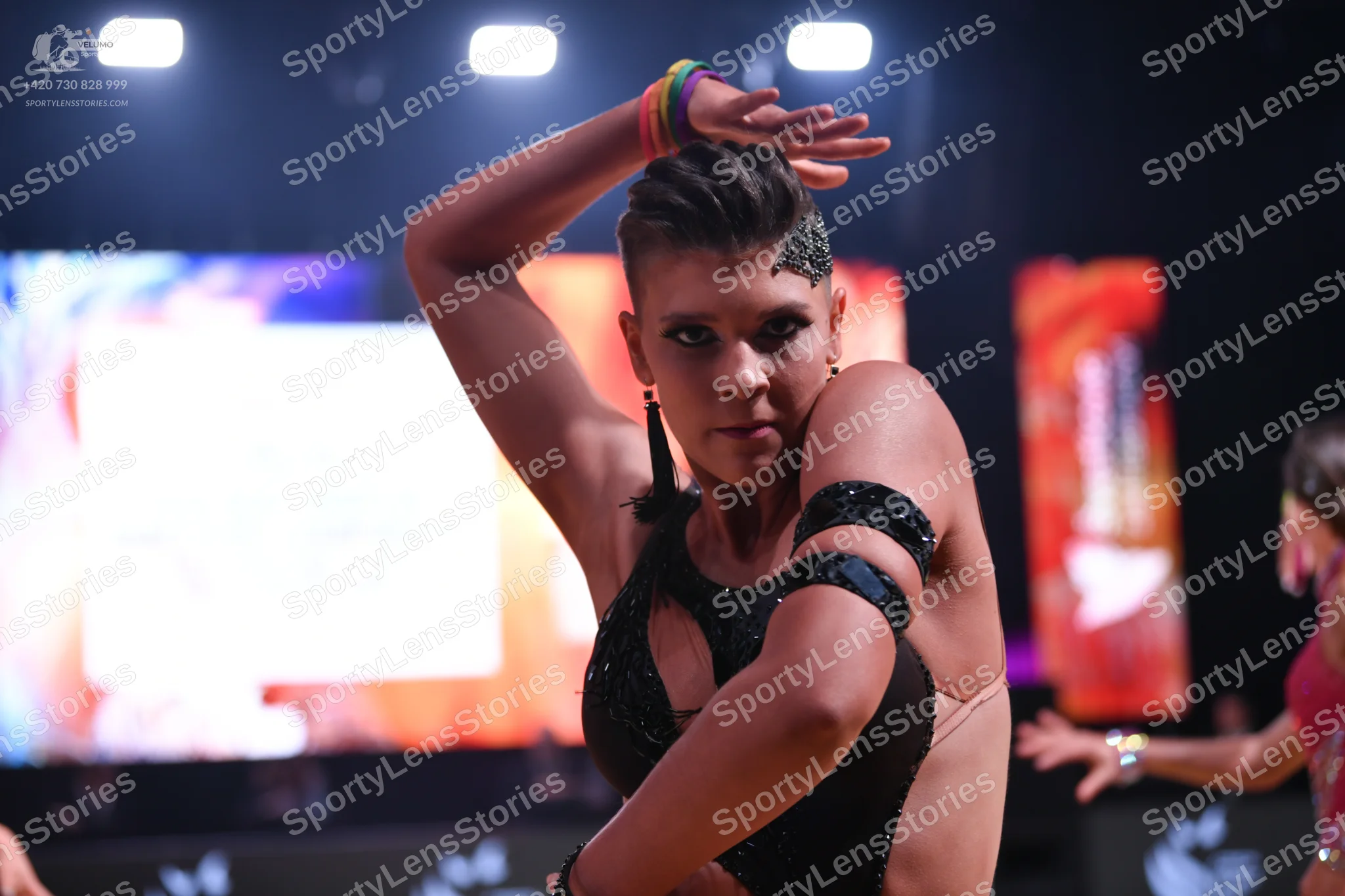 Dancesport competitor: Female dancer in foreground: black latin dress with small sequins and black band