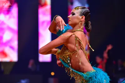Dancesport competitor: Female dancer: Gold sequined Latin costume with teal feather and fringe accents,