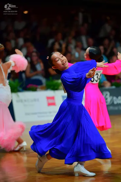 Dancesport competitor: Female dancer in blue: royal blue ballroom dress with long sleeves and a large, 
