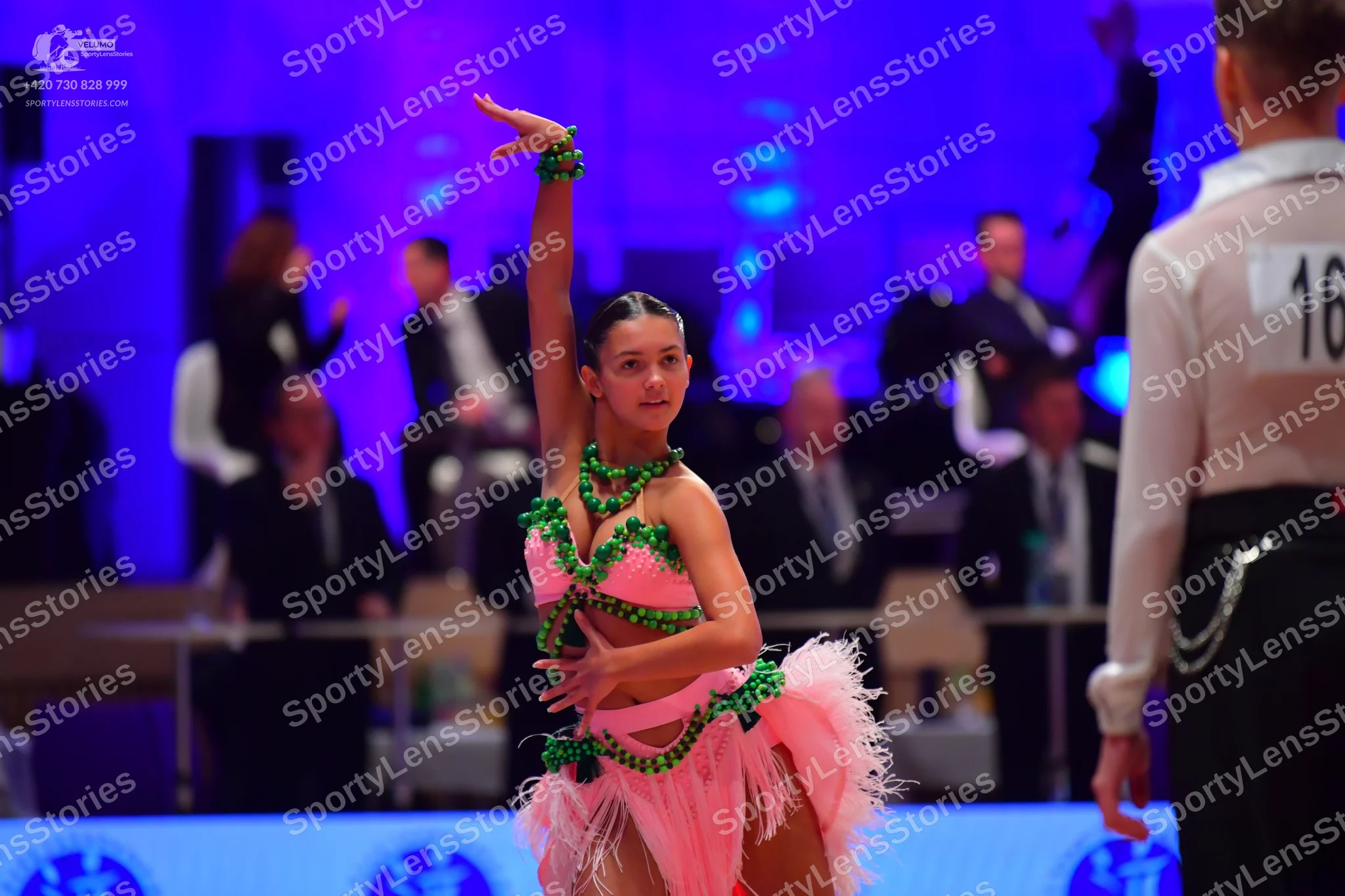 Dancesport competitor: Female dancer: pink Latin costume with green rhinestone embellishments and a pin