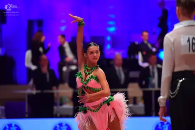 Dancesport competitor: Female dancer: pink Latin costume with green rhinestone embellishments and a pin