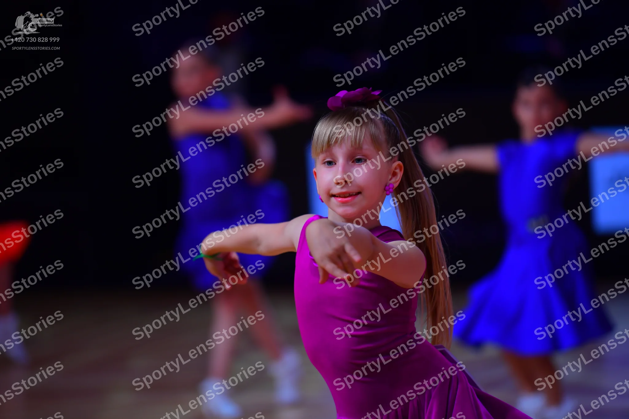 Dancesport competitor: Female dancer in foreground: bright magenta sleeveless dress made of smooth, str