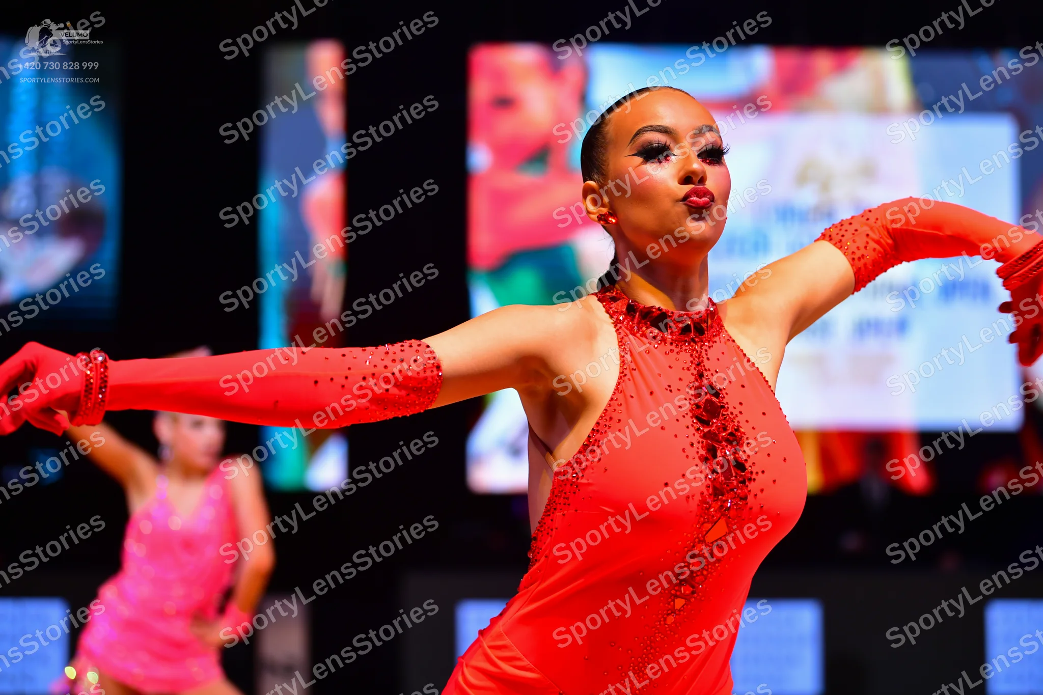 Dancesport competitor: Female dancer in foreground: red latin dress with sequin/beaded embellishments a