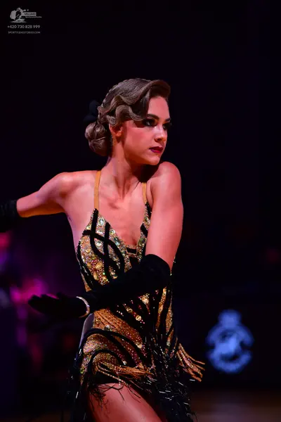 Dancesport competitor: Female dancer: gold and black latin dress with sequin patterns and black fringe,
