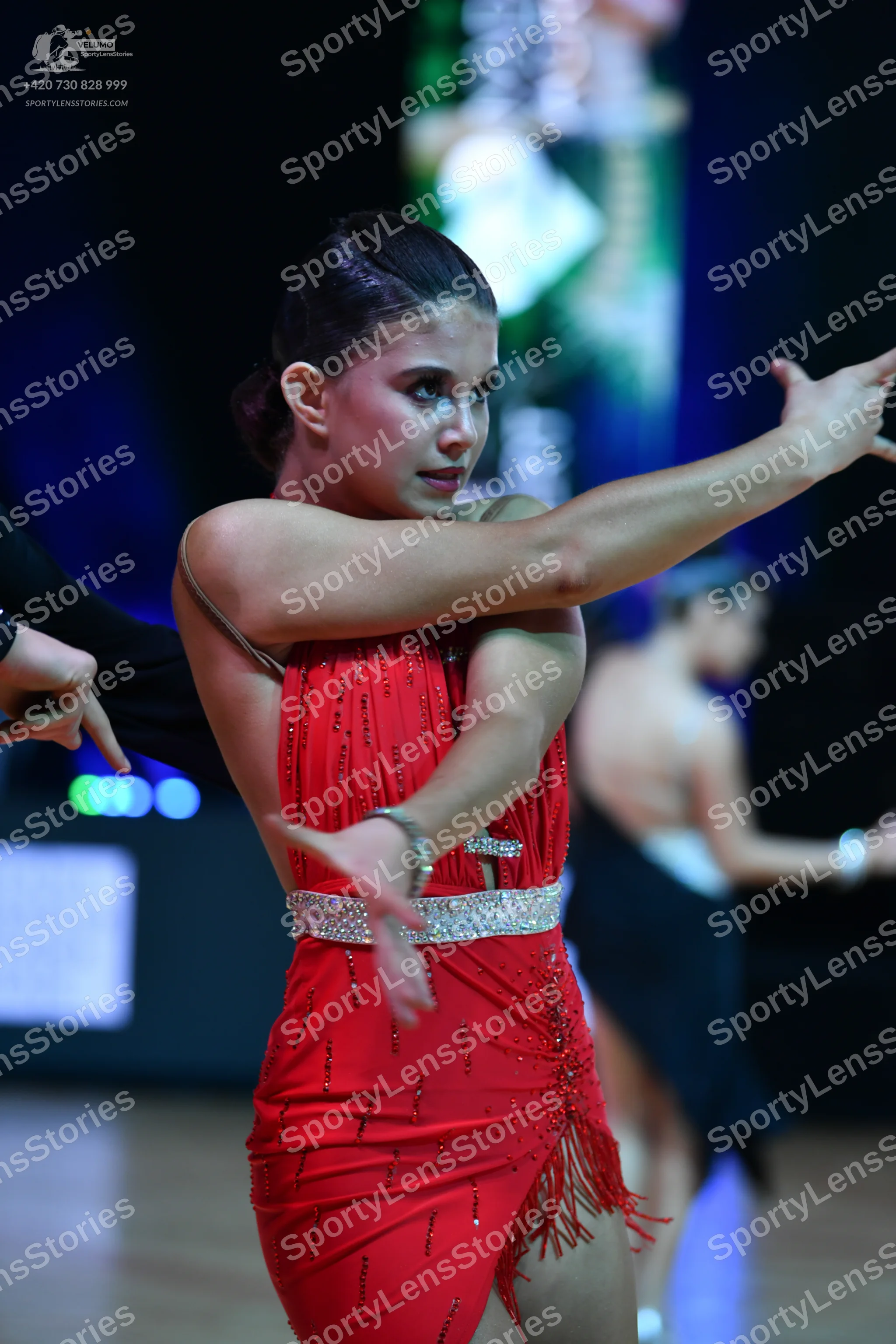 Dancesport competitor: Female dancer in foreground: red Latin dress with thin straps, a sparkly belt, a
