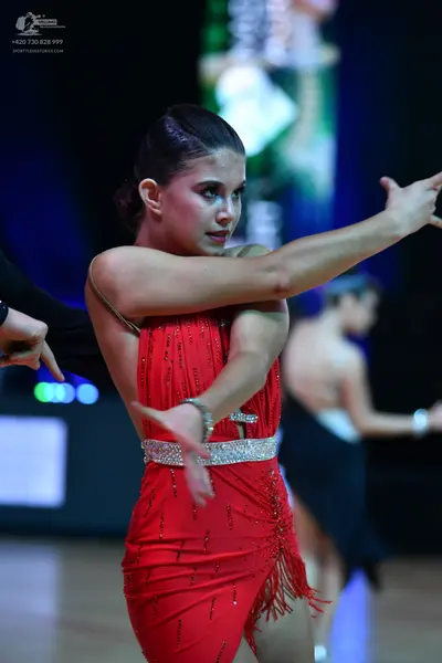 Dancesport competitor: Female dancer in foreground: red Latin dress with thin straps, a sparkly belt, a