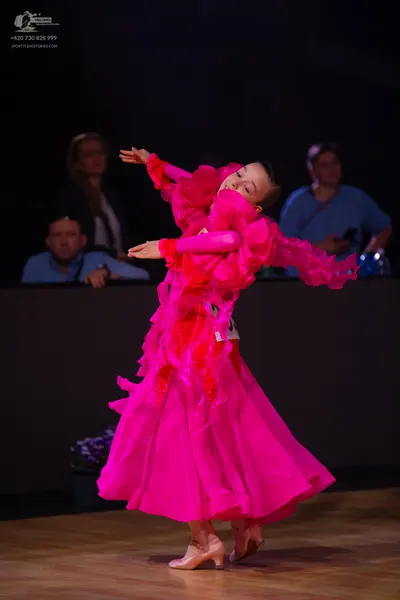 Dancesport competitor: Female dancer: bright pink ballgown with voluminous ruffled layers of fabric and