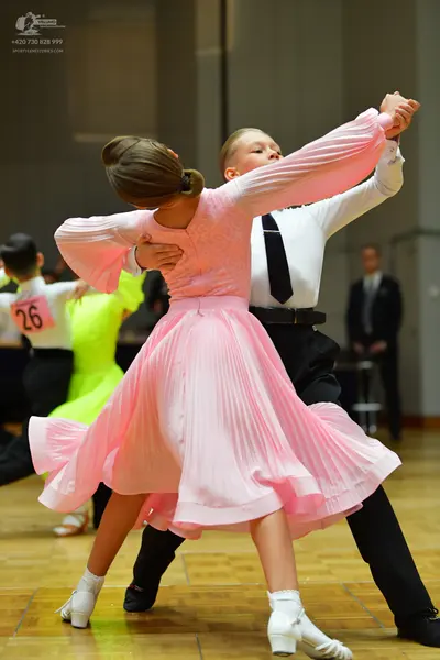 Dancesport competitor #26: Foreground female dancer: light pink, long-sleeved, pleated flowing skirt