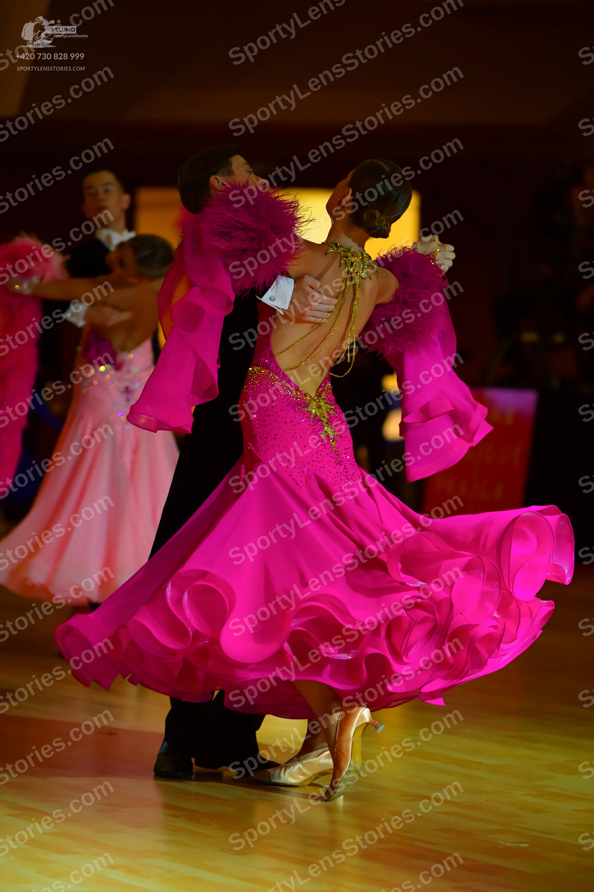 Dancesport competitor: Foreground female dancer: bright pink ballroom dress with a voluminous, ruffled
