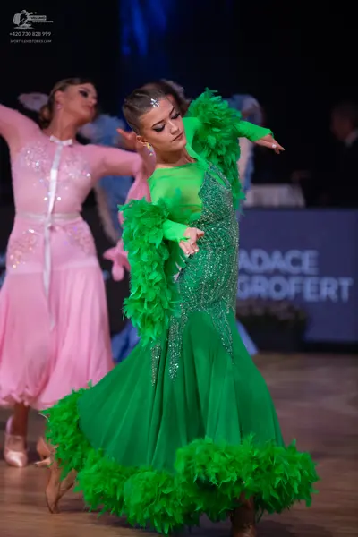 Dancesport competitor: Female dancer 1: green Latin dance dress with feathered sleeves and hem, and a s