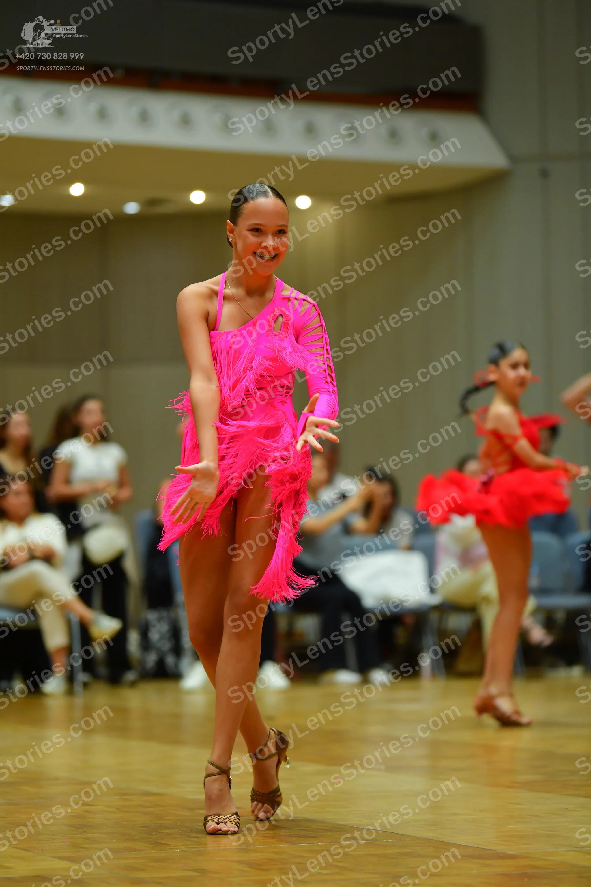 Dancesport competitor: Female dancer 1: bright pink latin dance dress with long sleeves and fringe
