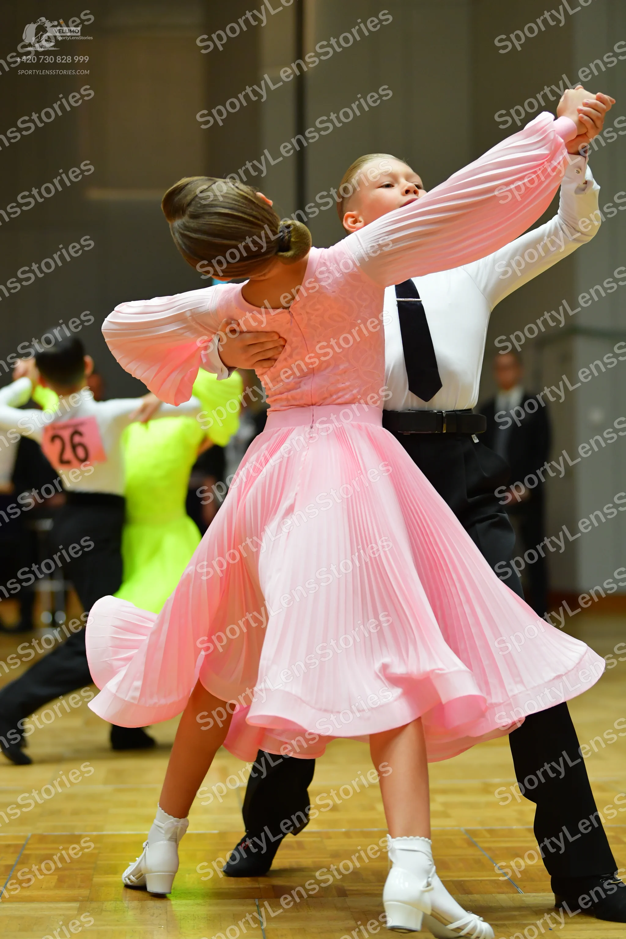 Dancesport competitor #26: Female dancer in foreground: pink long-sleeved dress with a pleated skirt and wh