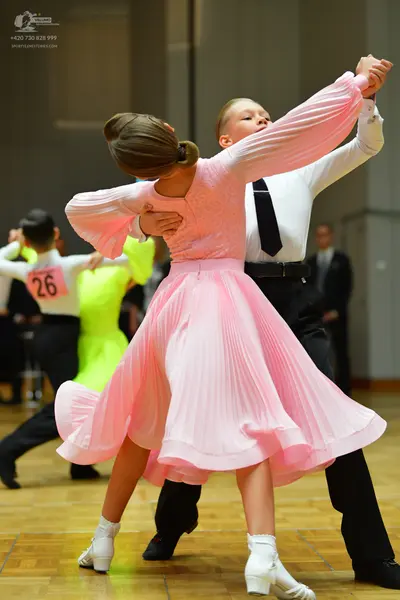 Dancesport competitor #26: Female dancer in foreground: pink long-sleeved dress with a pleated skirt and wh