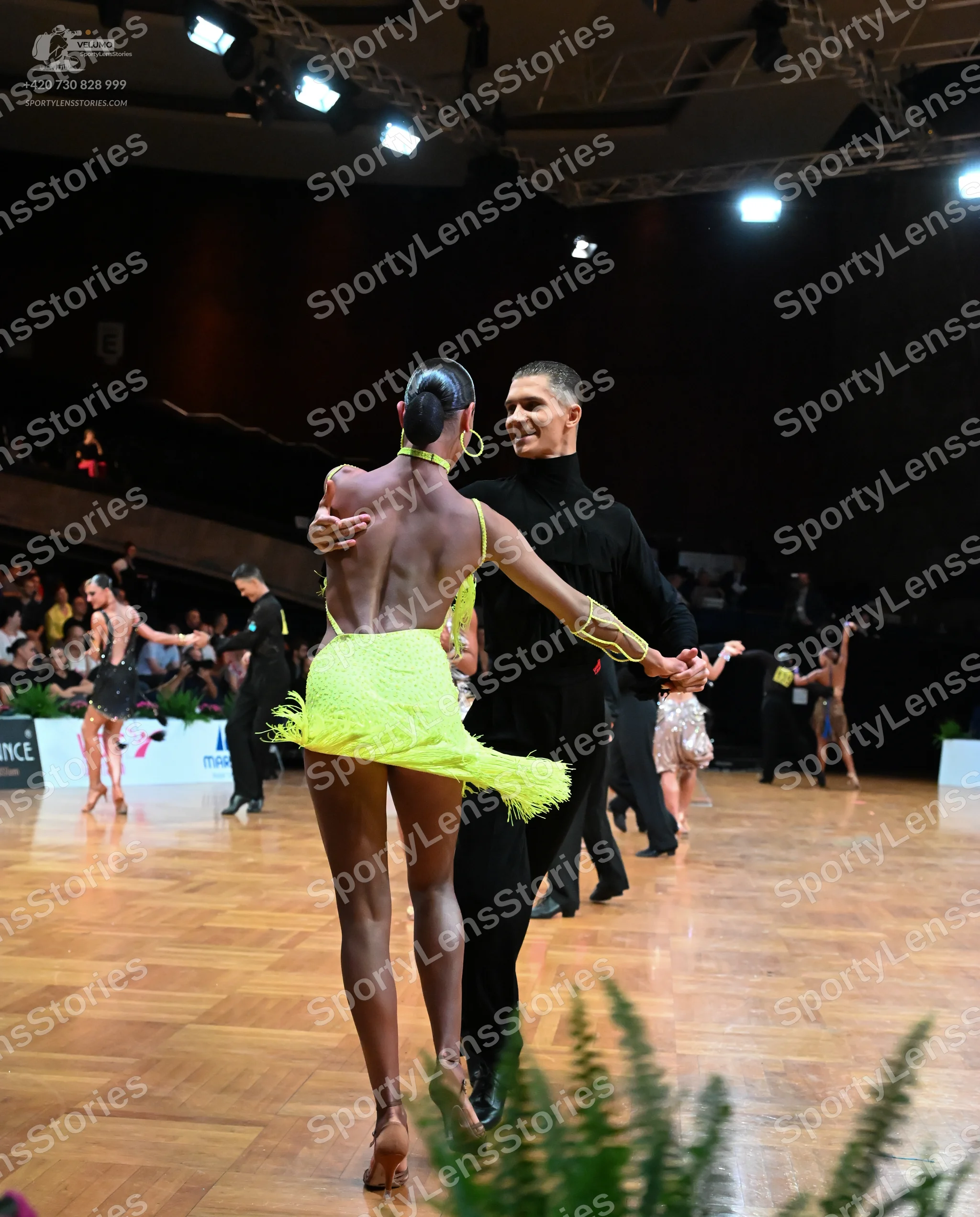 Dancesport competitor: Foreground female dancer: yellow latin dress with fringe