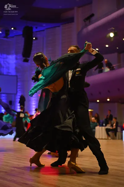 Dancesport competitor: Female dancer: dark, voluminous ballgown with flowing fabric and teal accents