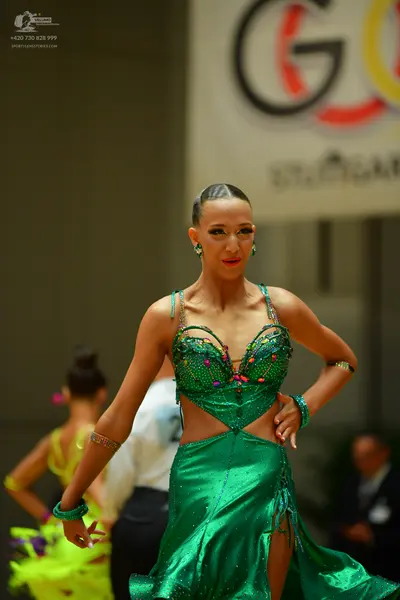 Dancesport competitor: Female dancer (foreground): emerald green Latin dance dress with a cut-out waist