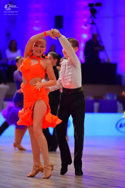 Dancesport competitor: Female dancer: bright orange Latin dance dress with cutouts and a ruffled skirt,