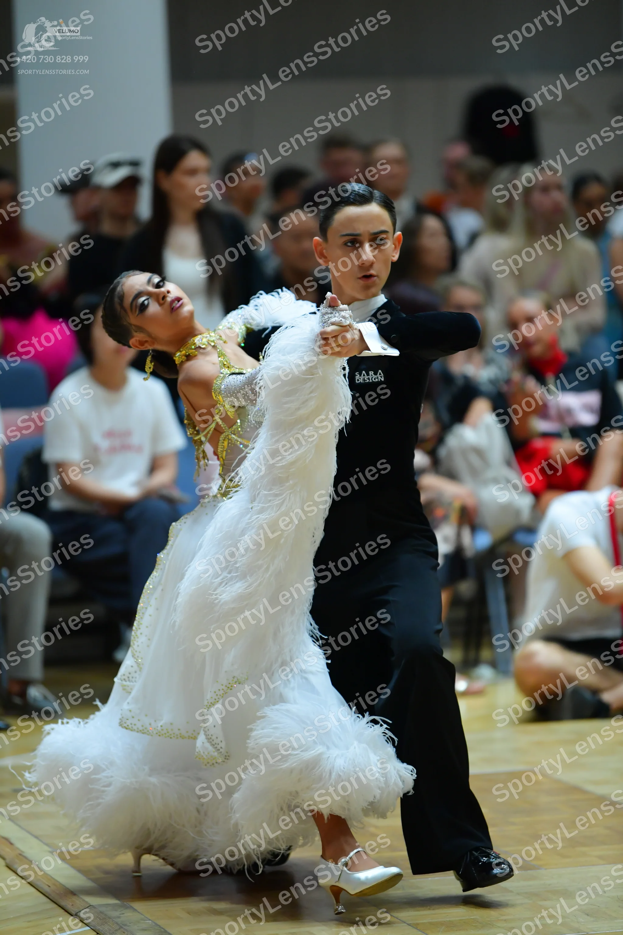 Dancesport competitor: Female dancer: voluminous white ballroom gown with feather-like textures and gol