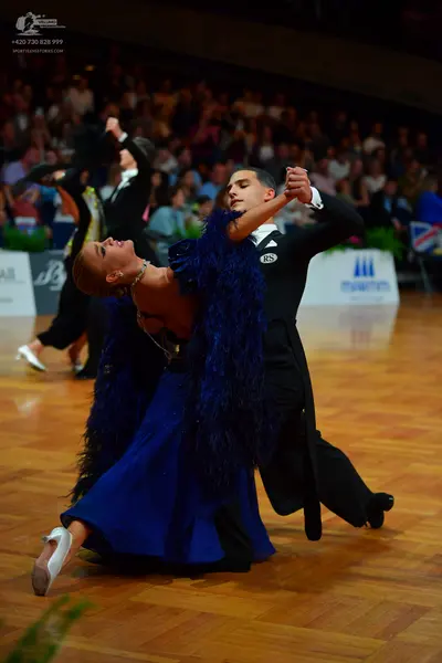 Dancesport competitor: Foreground female dancer: deep blue ballgown with large dark blue feathery/fring