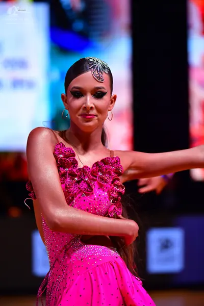 Dancesport competitor: Female dancer: bright pink latin dress decorated with rhinestones and large 3D f