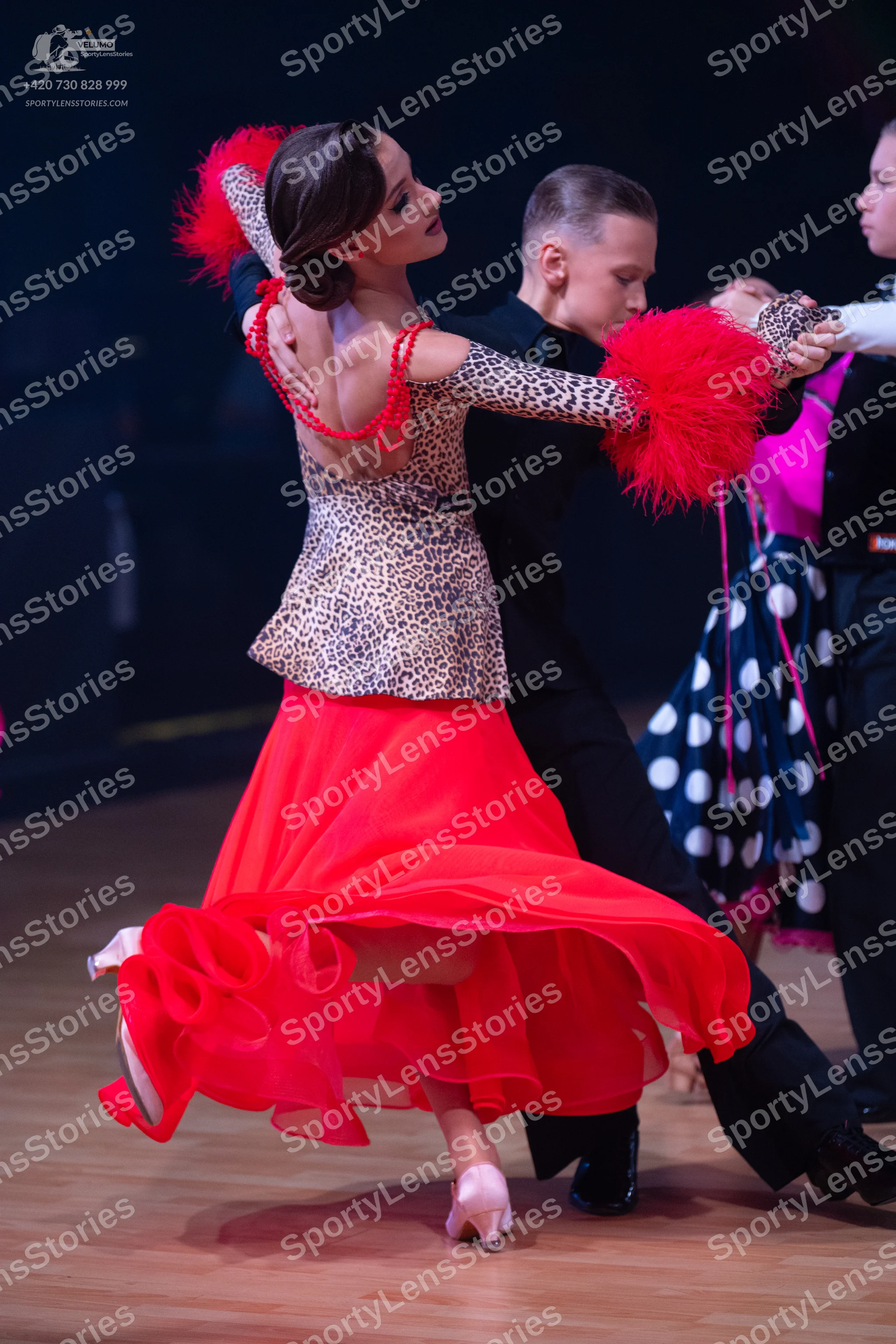 Dancesport competitor: Female dancer: leopard print long-sleeved top with large red feathery accents on