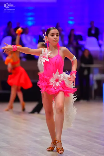 Dancesport competitor: Main female dancer: bright pink latin dress with white floral embellishments and