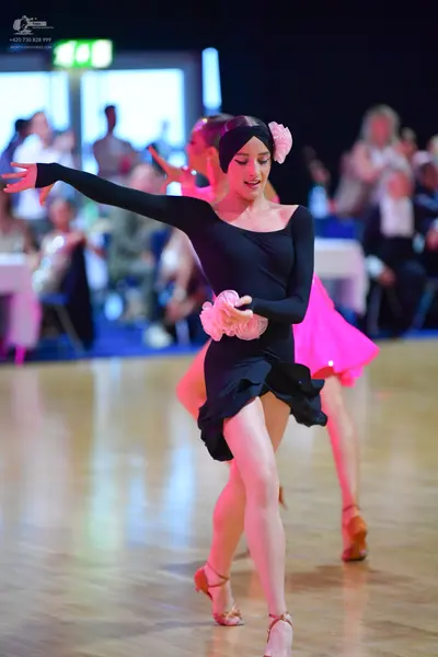 Dancesport competitor: Female dancer (foreground): black long-sleeved latin dress with a pink floral ac