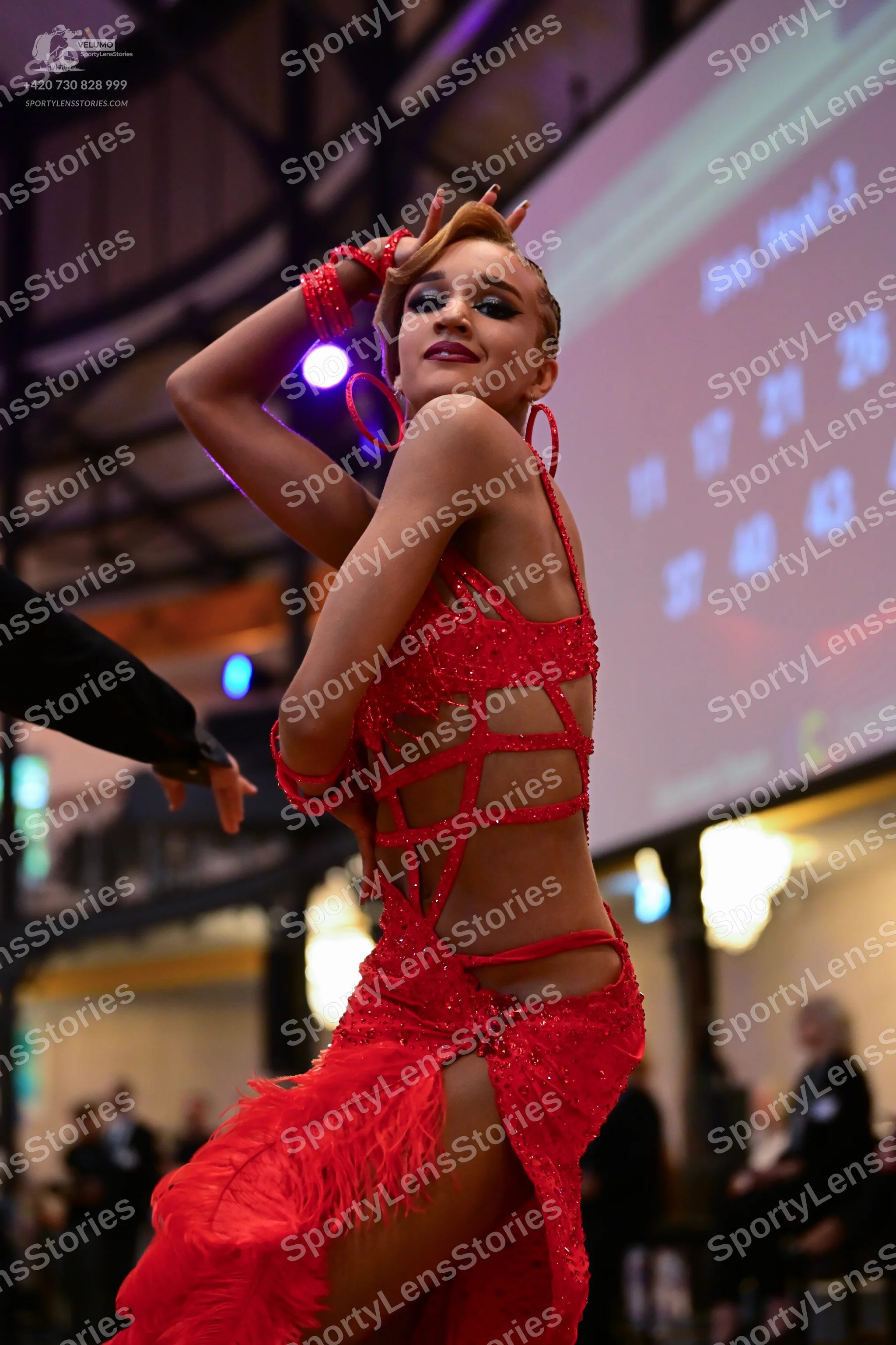 Dancesport competitor: Female dancer: red latin dress with sequins, cutout straps, and fringe, accompan