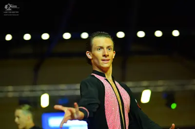 Dancesport competitor: Male dancer in foreground: black long-sleeved shirt with a pink sequined panel d