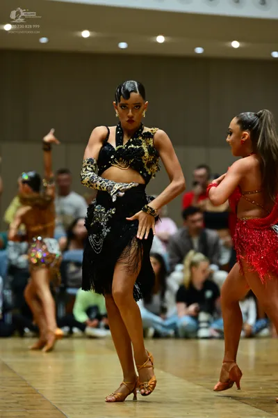 Dancesport competitor: Female dancer (center): black and gold Latin dance dress with sequin and bead em