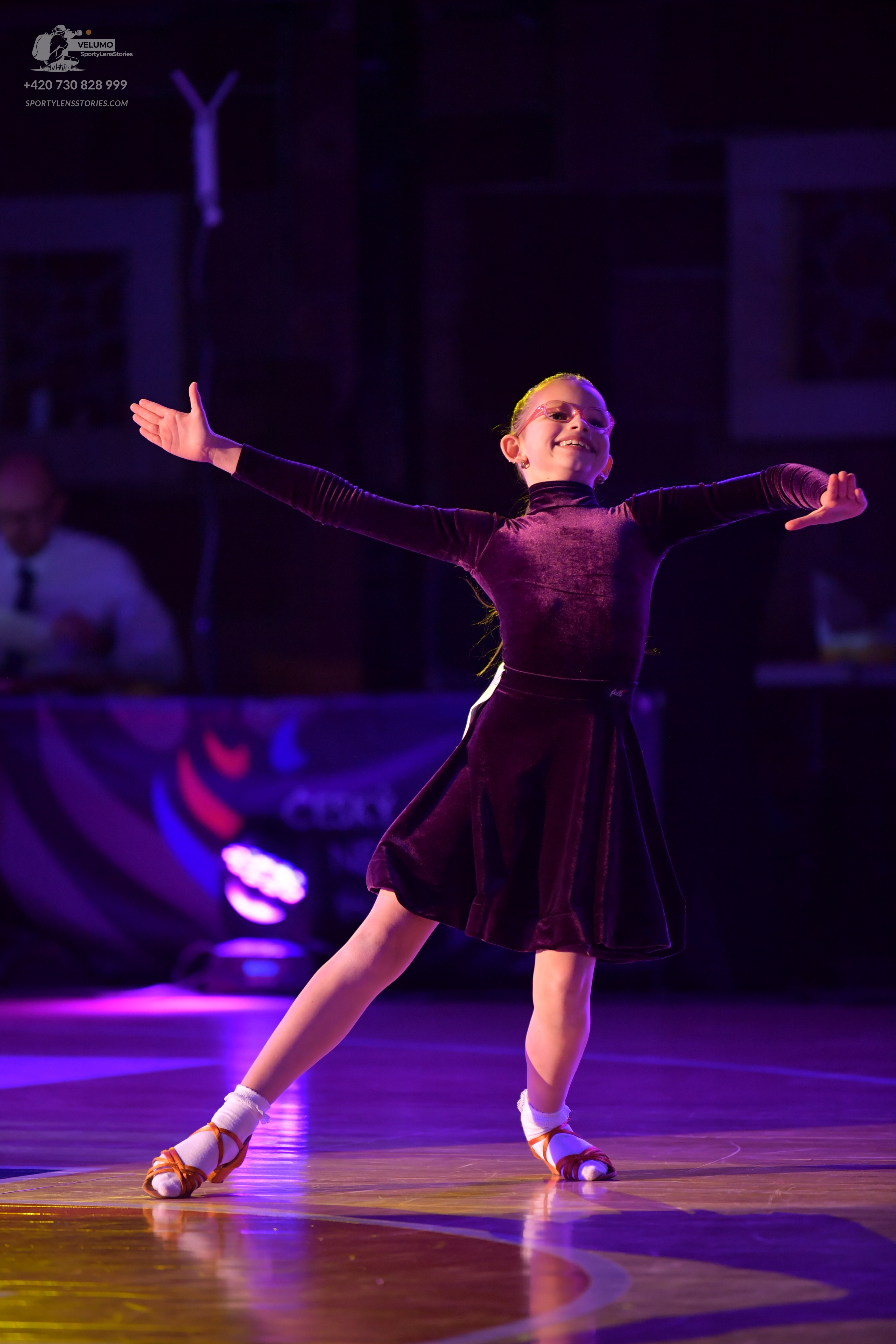 Dancesport competitor: Female dancer: dark purple velvet long-sleeved dress with a flared skirt, worn w