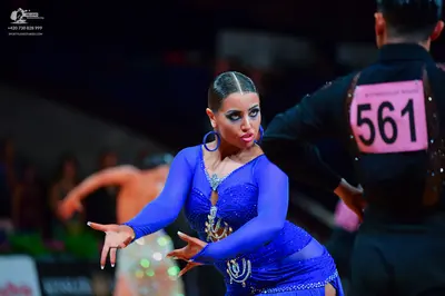 Dancesport competitor: Female dancer: royal blue long-sleeved latin dress with sequins and large blue h