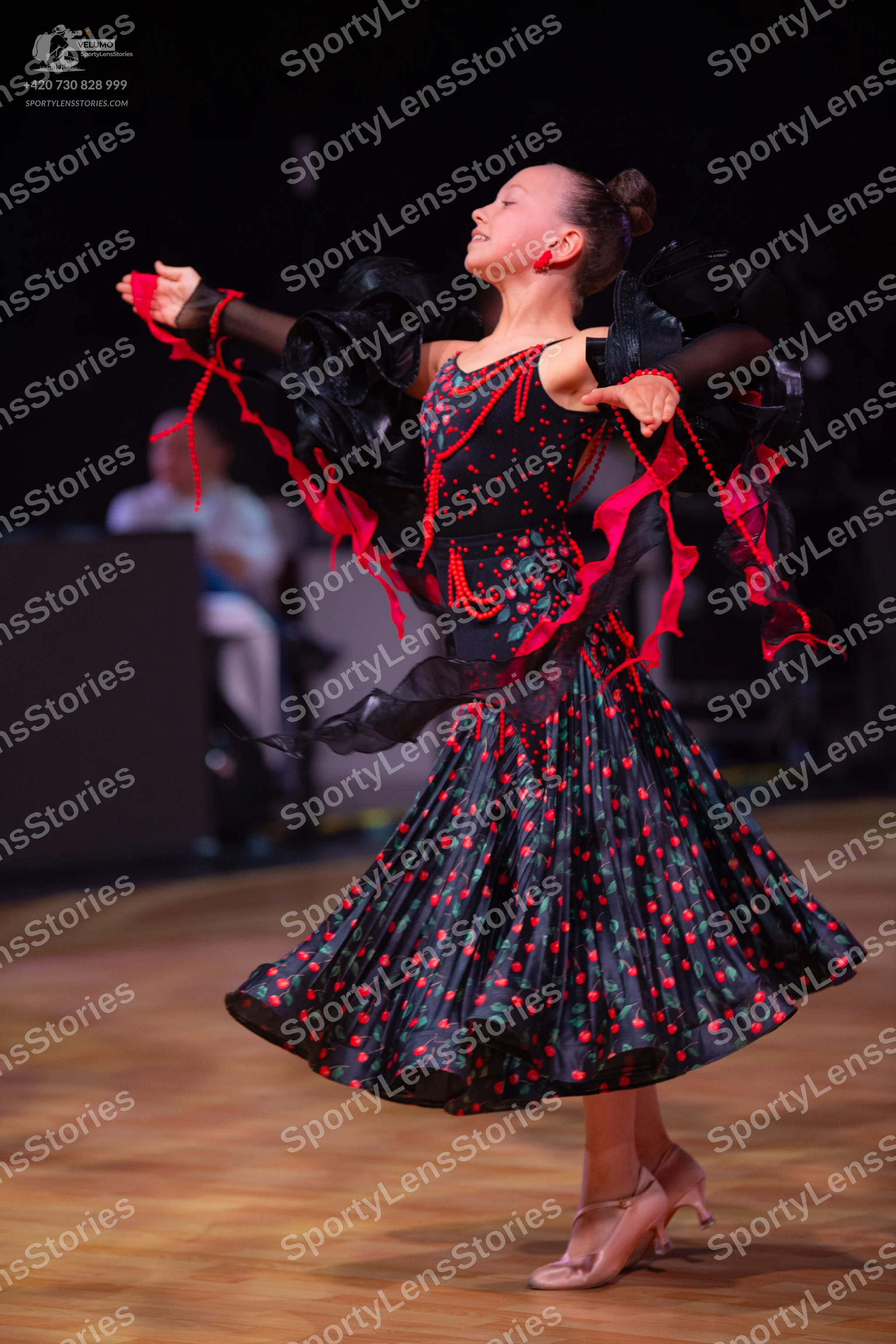 Dancesport competitor: Female dancer: black dress with red floral or polka dot pattern, large black ruf