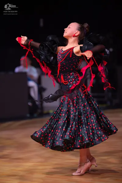 Dancesport competitor: Female dancer: black dress with red floral or polka dot pattern, large black ruf