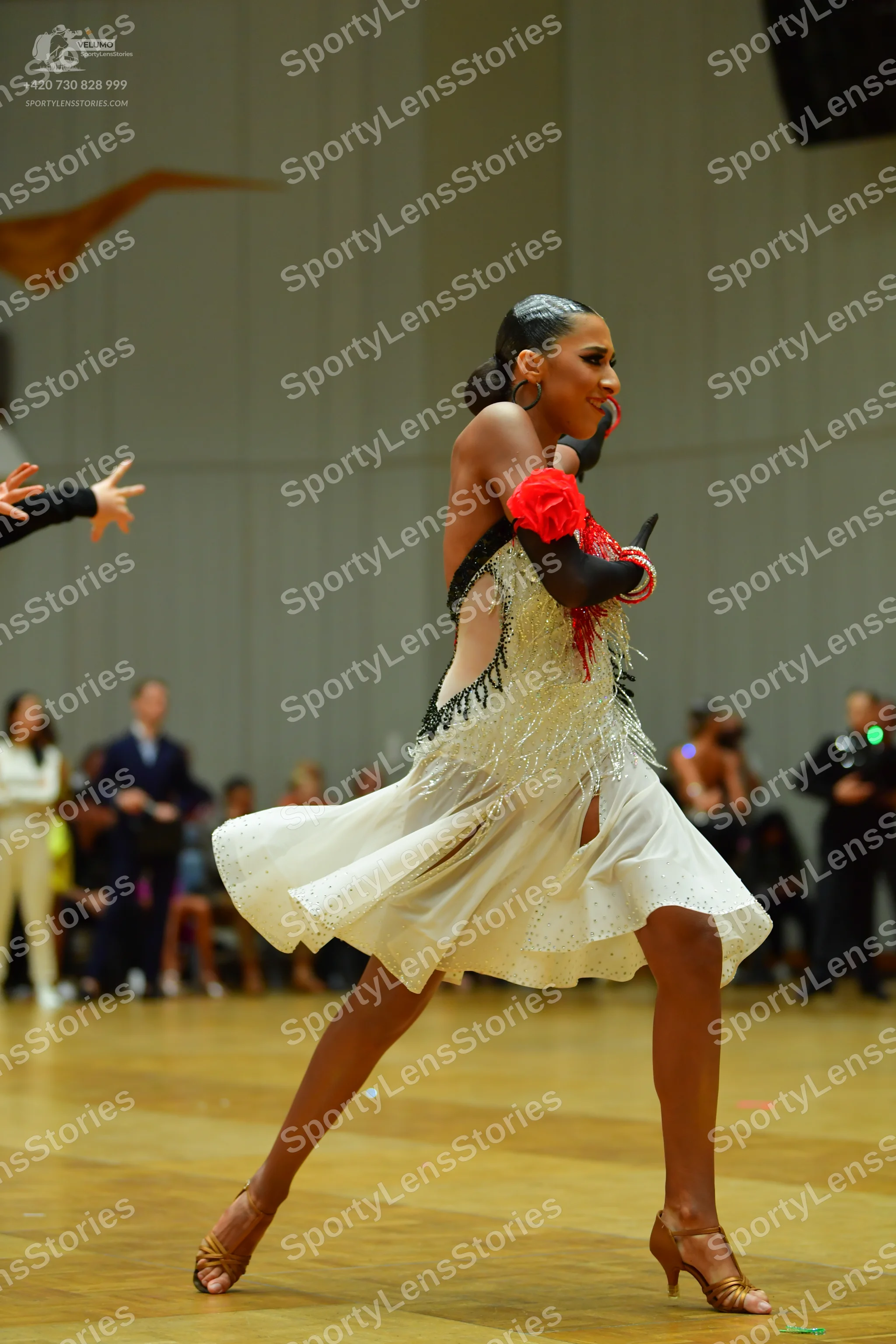 Dancesport competitor: Female dancer: cream-colored Latin dress with black beaded trim, red floral arm