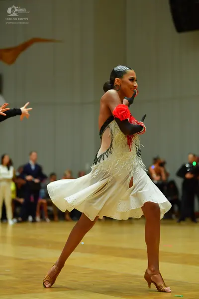Dancesport competitor: Female dancer: cream-colored Latin dress with black beaded trim, red floral arm 