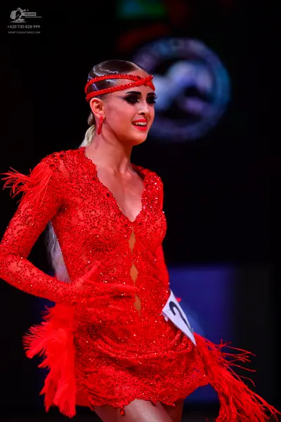Dancesport competitor: Female dancer: red latin dress with sequins, long sleeves, deep V-neck, and frin