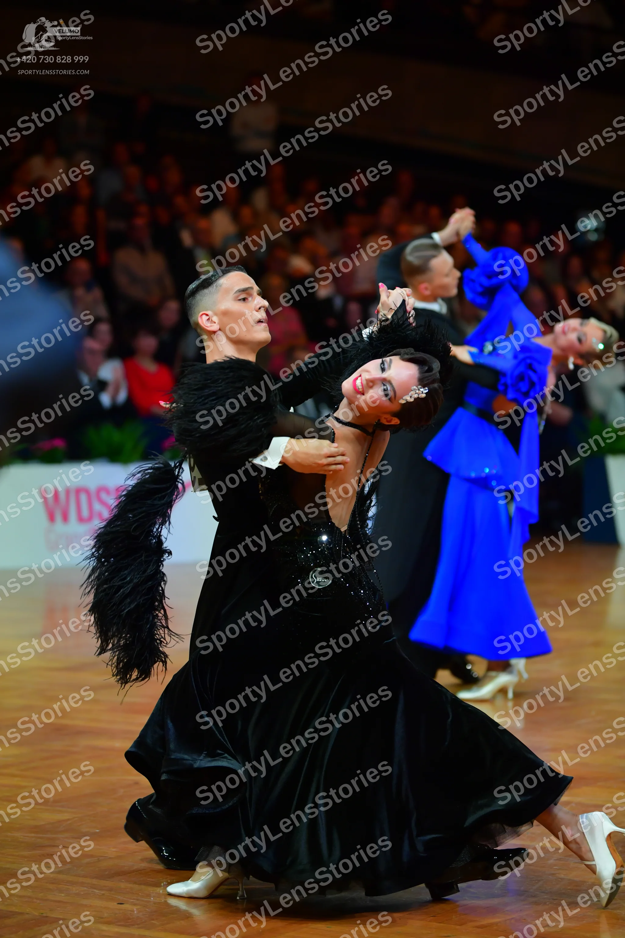 Dancesport competitor: Female dancer in foreground: black ballroom gown with large black feather trim o