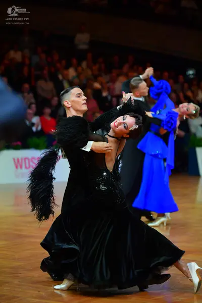 Dancesport competitor: Female dancer in foreground: black ballroom gown with large black feather trim o