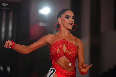 Dancesport competitor: Female dancer: red latin dress with lace, sequins, and cutouts, accessorized wit