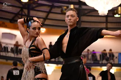 Dancesport competitor #24: Female dancer: black latin dress with gold sequin patterns and long fringe, with