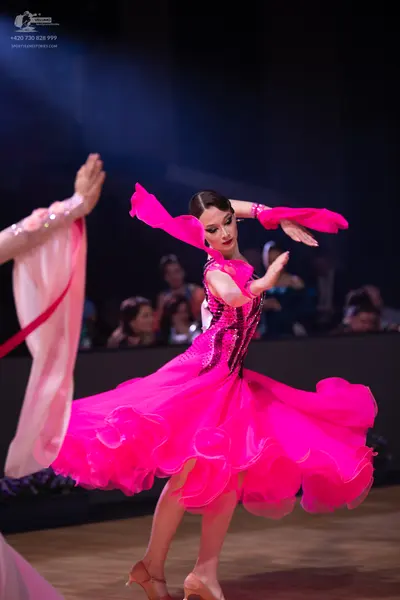 Dancesport competitor: Female dancer: bright pink ballroom dress with a voluminous, ruffled skirt, a bo