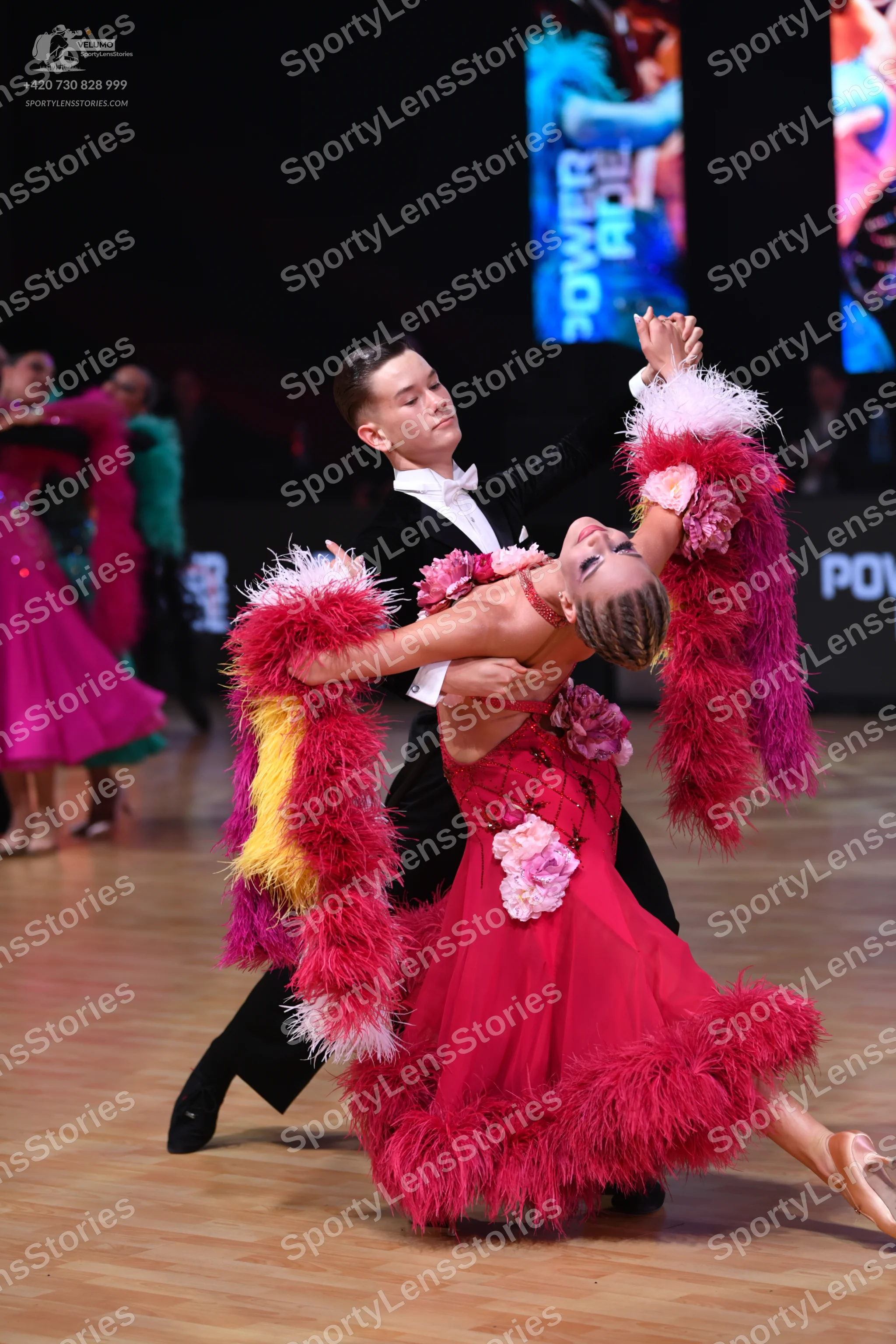 Dancesport competitor: Female dancer: red Latin dress with large pink floral appliqués on the bodice an