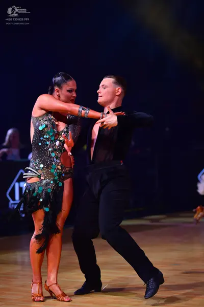 Dancesport competitor: Female dancer: dark green/black Latin dress heavily embellished with large teal 